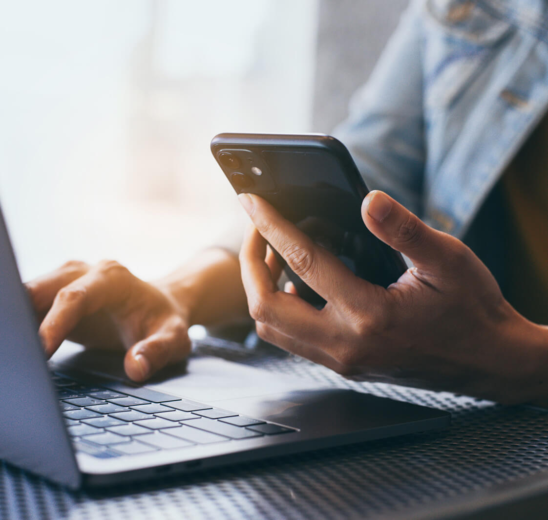 Person using mobile phone while on a laptop.