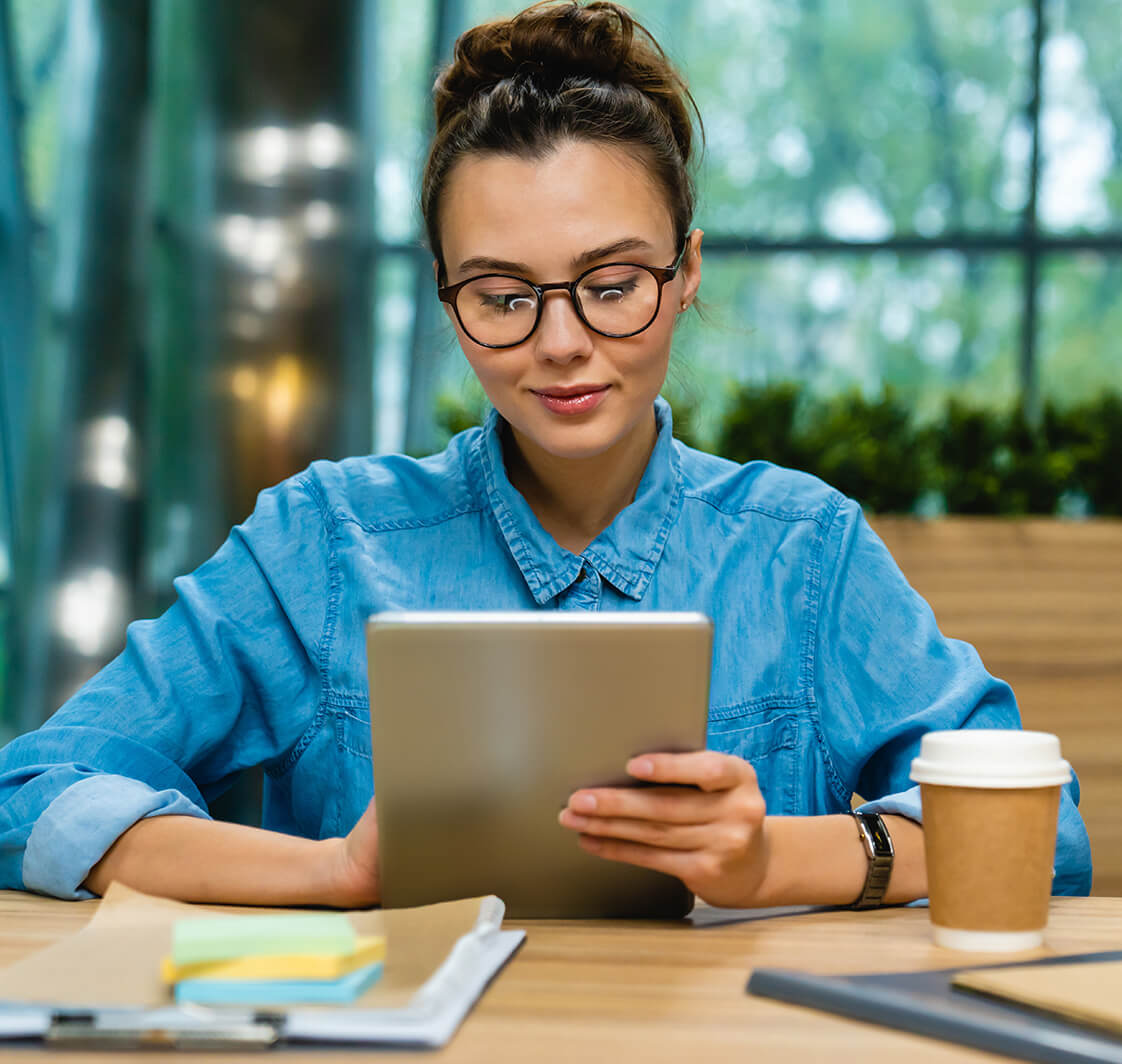 Nice-looking young caucasian businesswoman using tablet at the desk in modern office