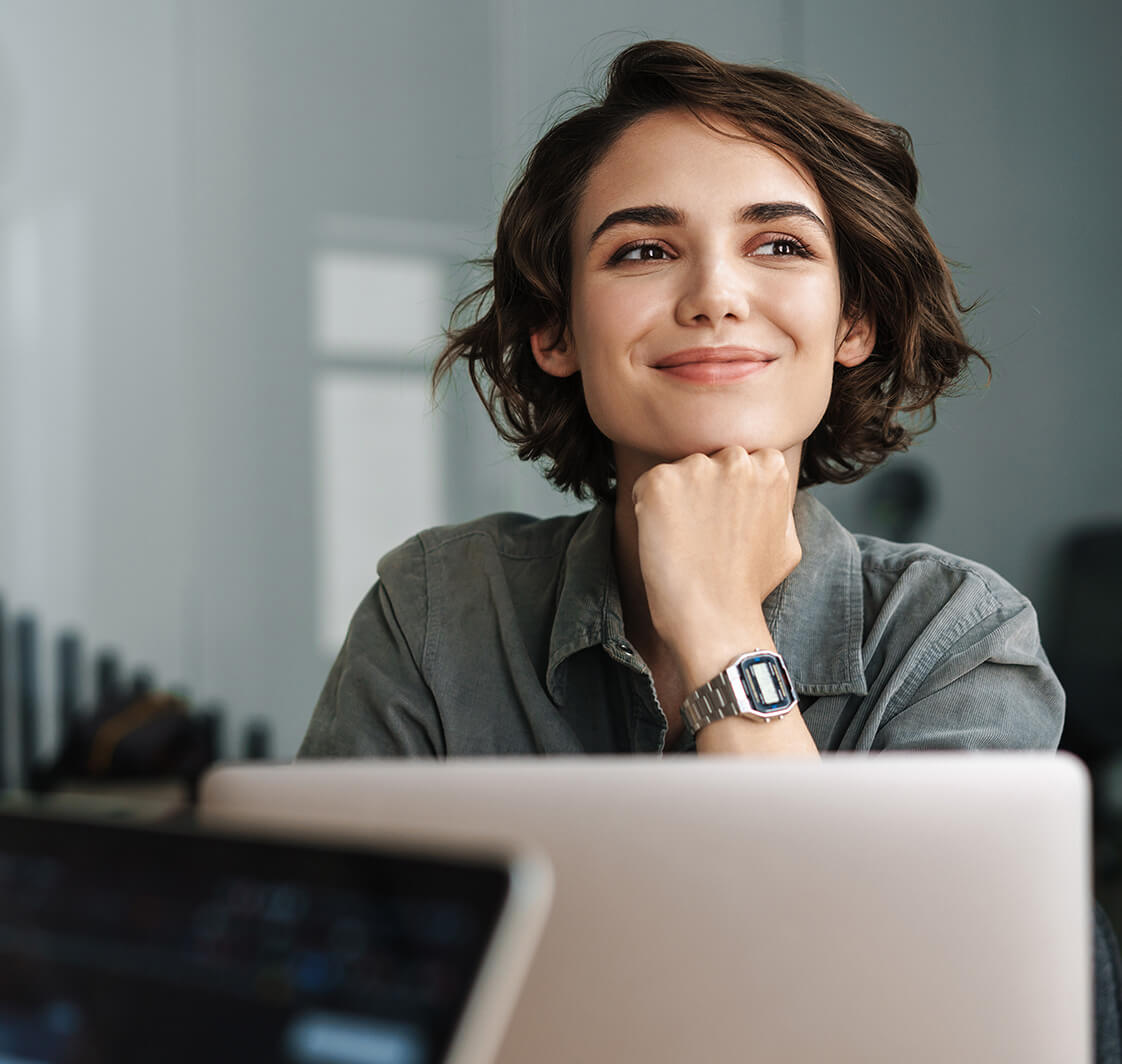 Image of young joyful woman smiling while working with laptop.