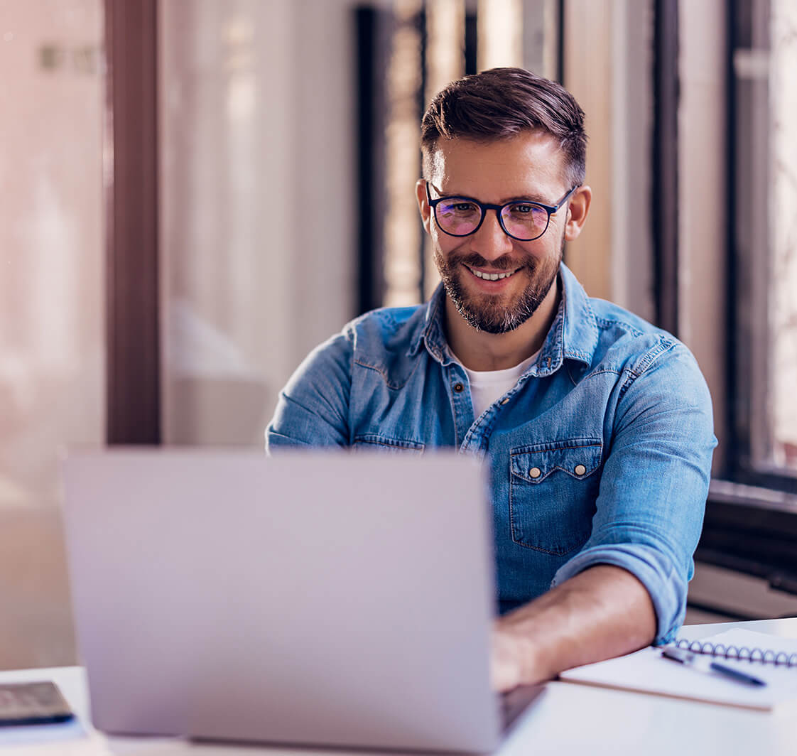 Smiling businessman sitting in office and working on laptop.