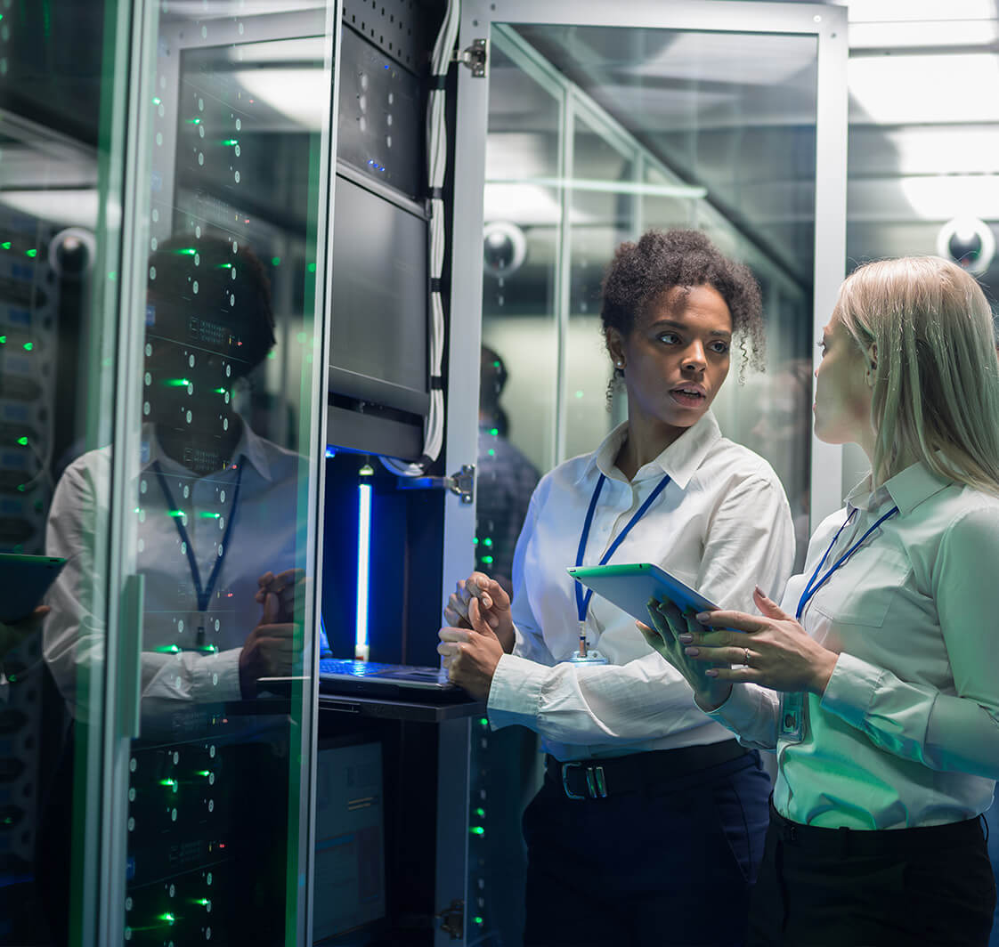 Two women are working in a data center with rows of server racks.