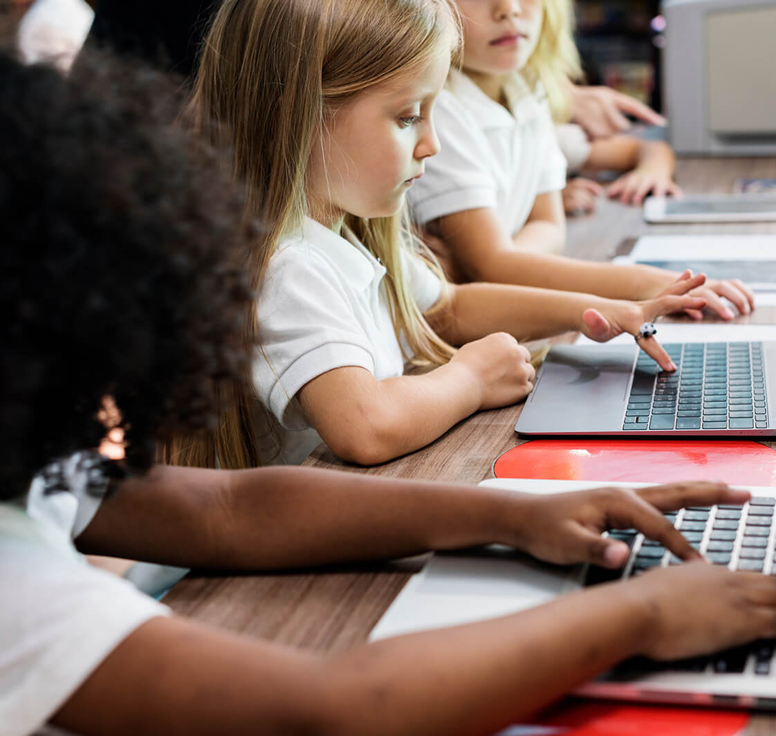 Happy kids at primary school using laptops.