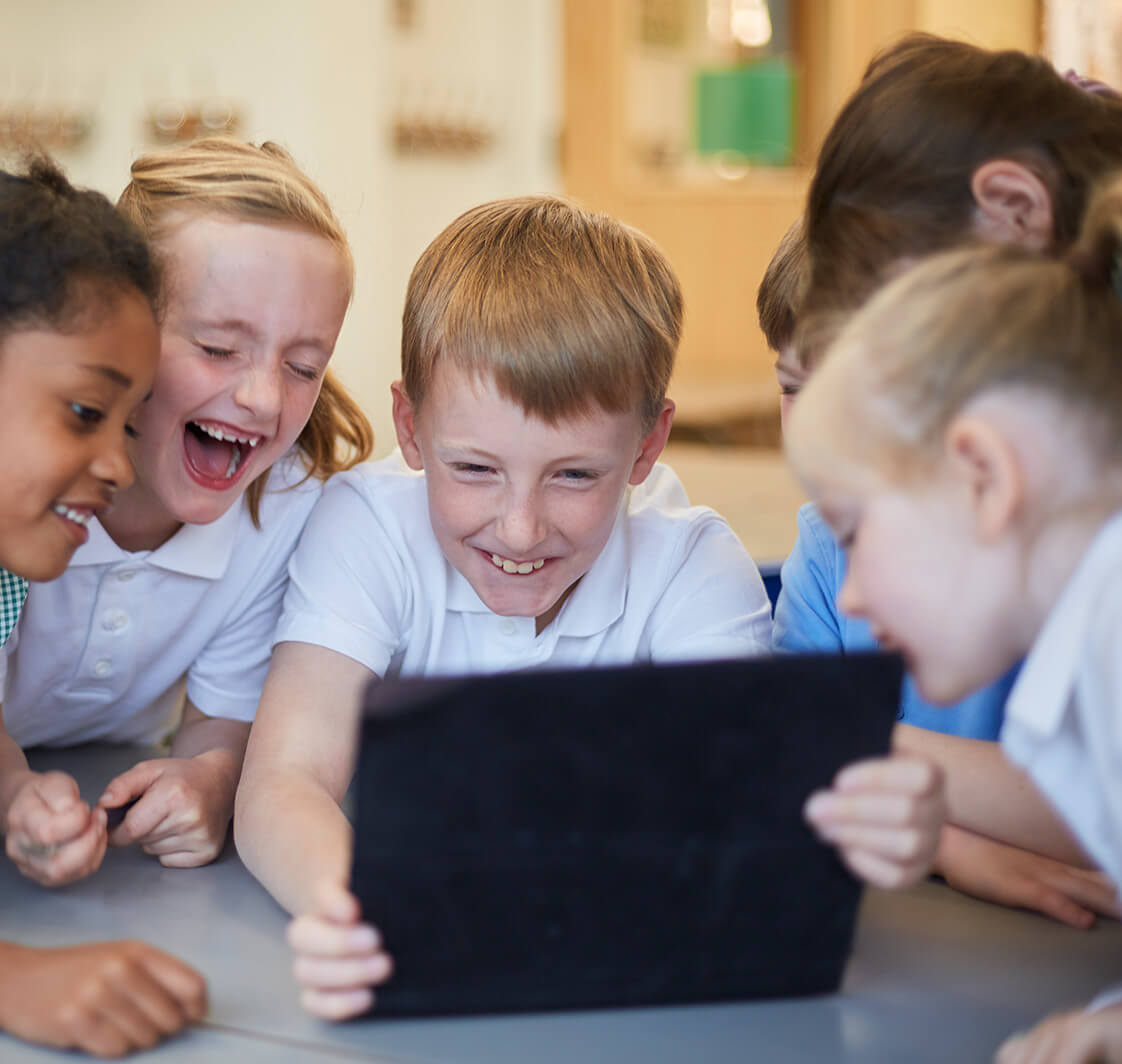 Schoolboys and girls laughing at digital tablet.