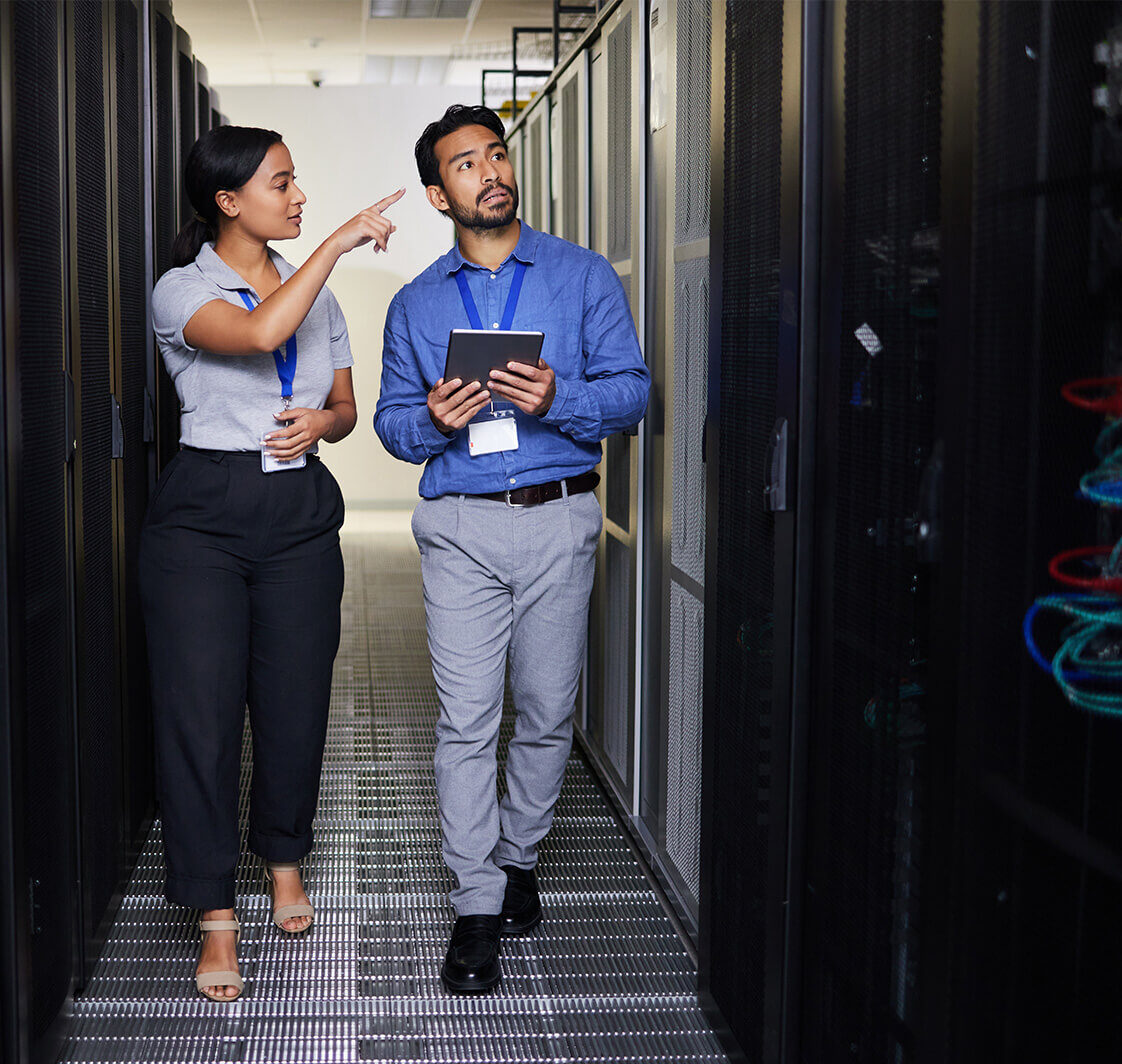IT Specialist Discusses Work with a Server Technician. They're Standing in Data Center.