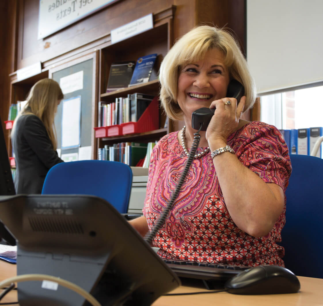 Smiling school secretary aswering the phone.