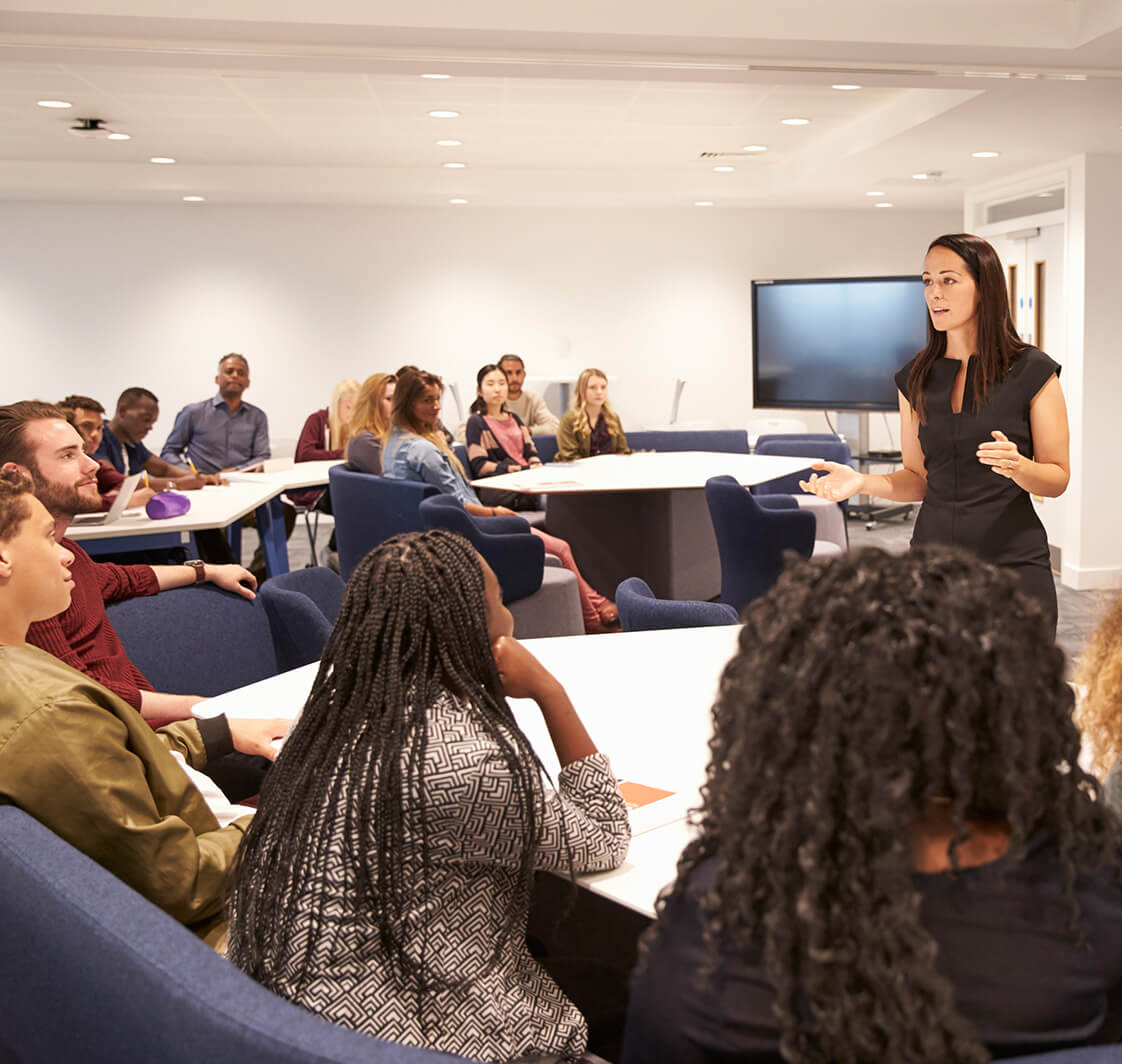 Higher education classroom with teacher presenting to a class of students.