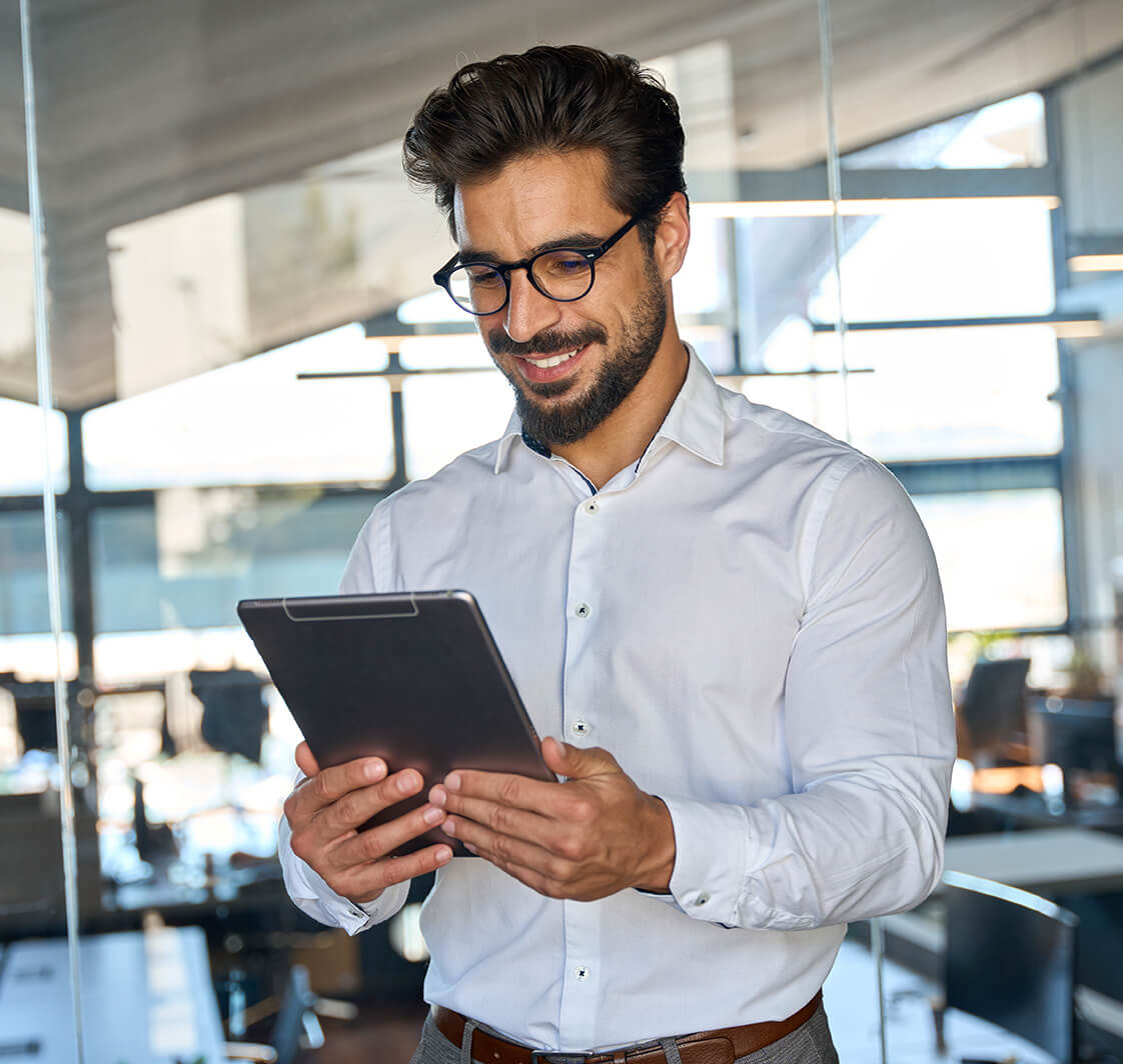 Smiling busy young Latin business man entrepreneur using tablet standing in office at work.