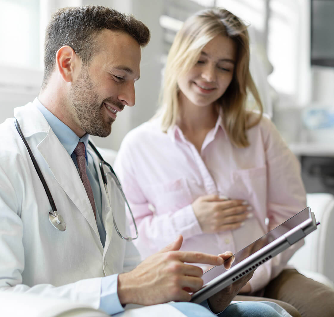 Male doctor showing tablet with healthcare results to young pregnant woman, digital technology and growth check