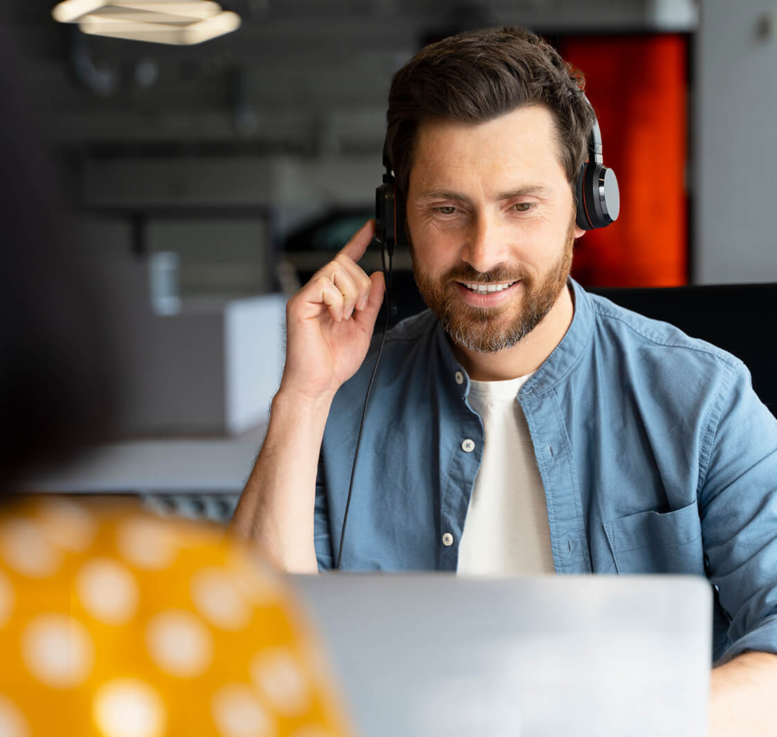 Smiling call center operator using laptop, answering call, communication with customer sitting in modern office.