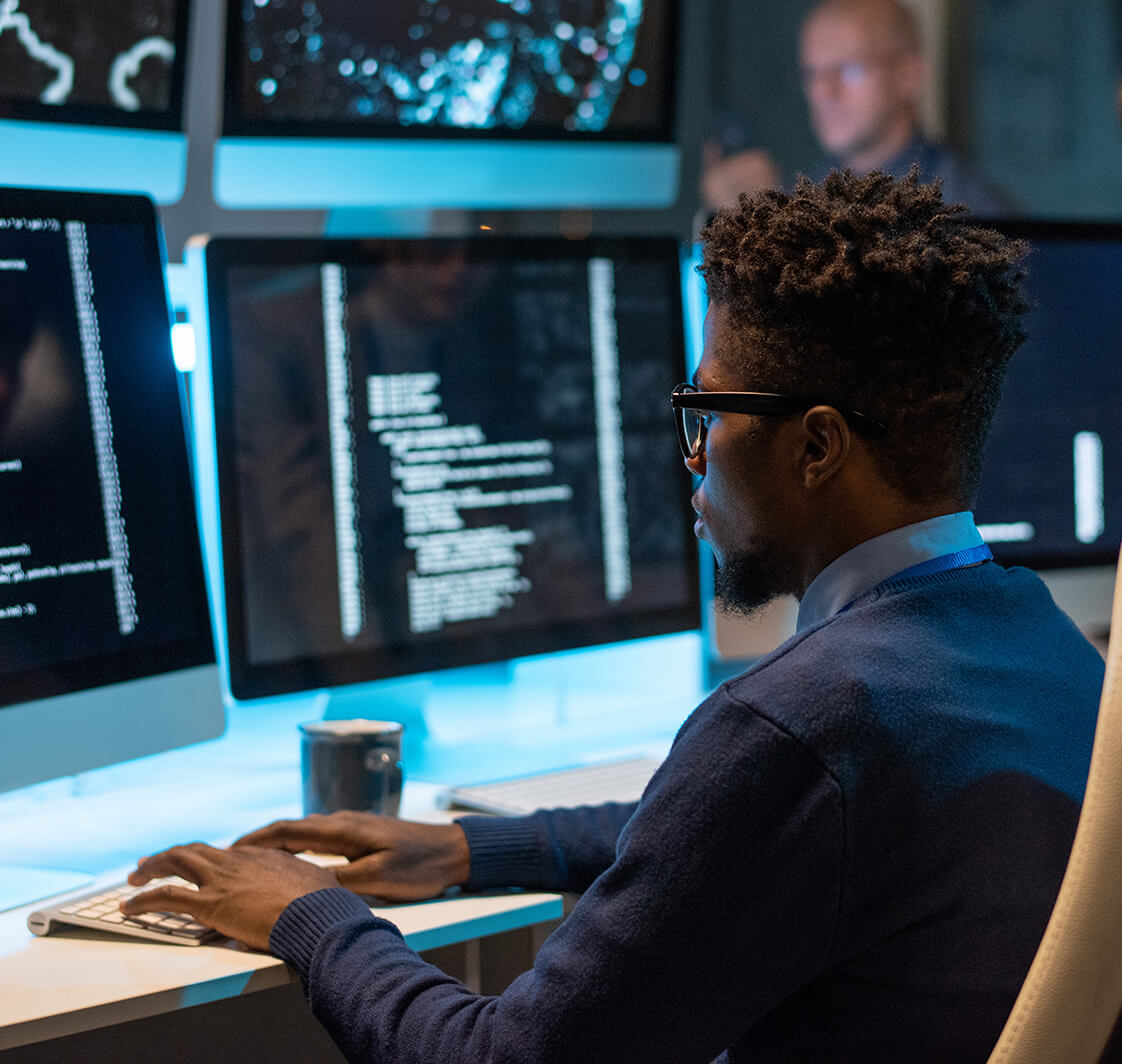 Young it-engineer decoding data while sitting in front of computer monitors and looking at screen of one of them.