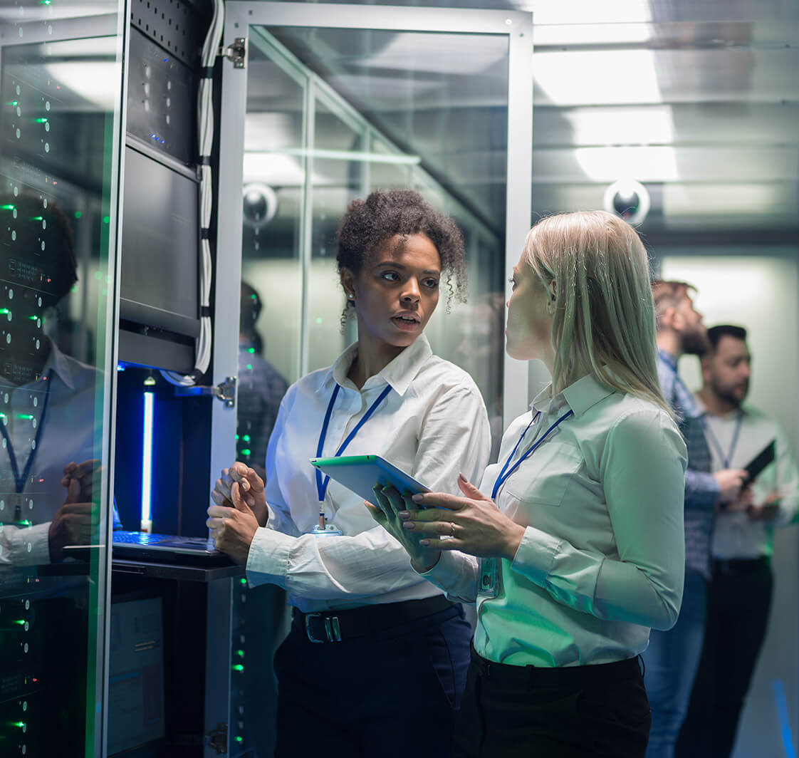 Two women are working in a data center with rows of server racks.