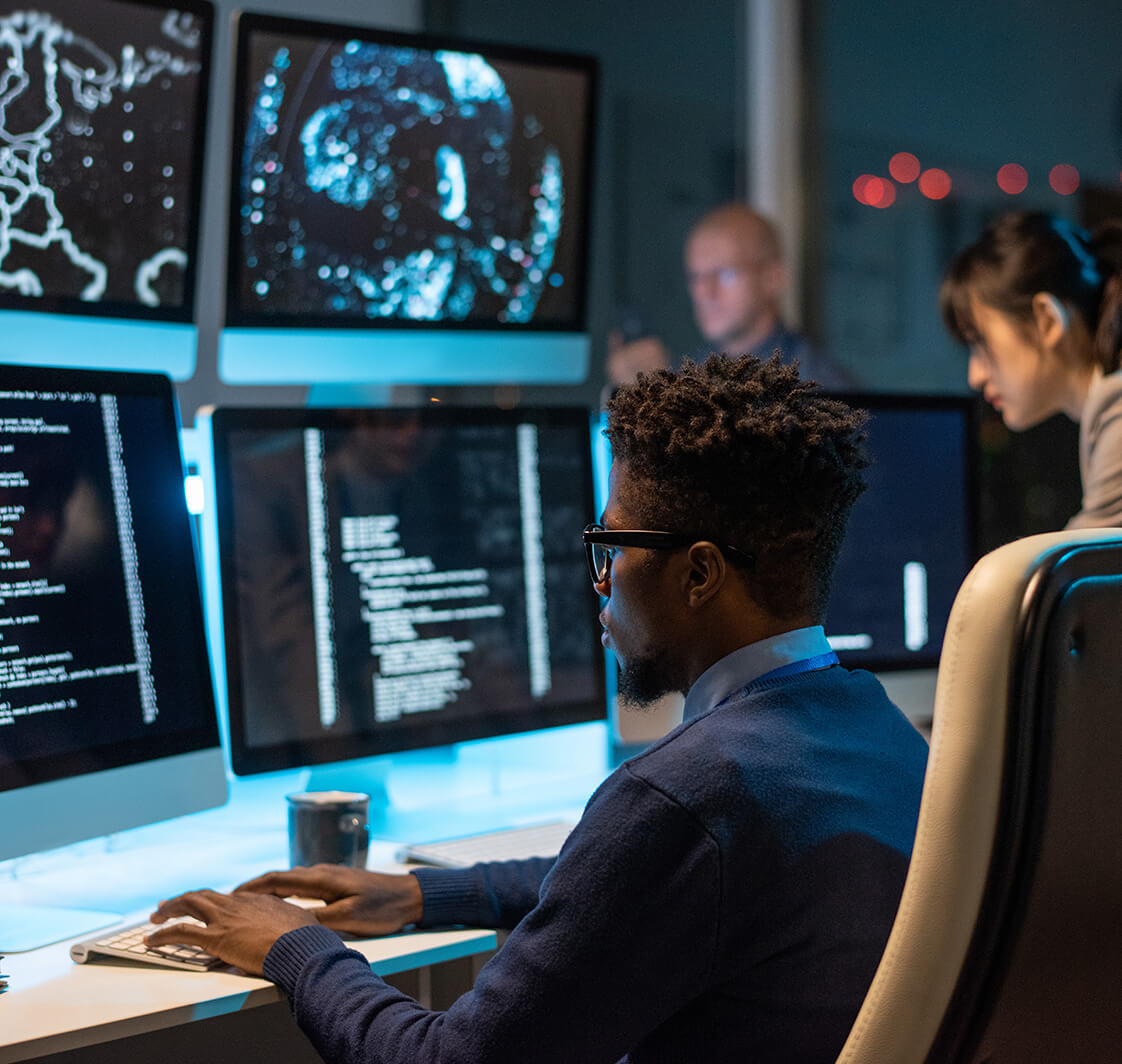 Young it-engineer decoding data while sitting in front of computer monitors.