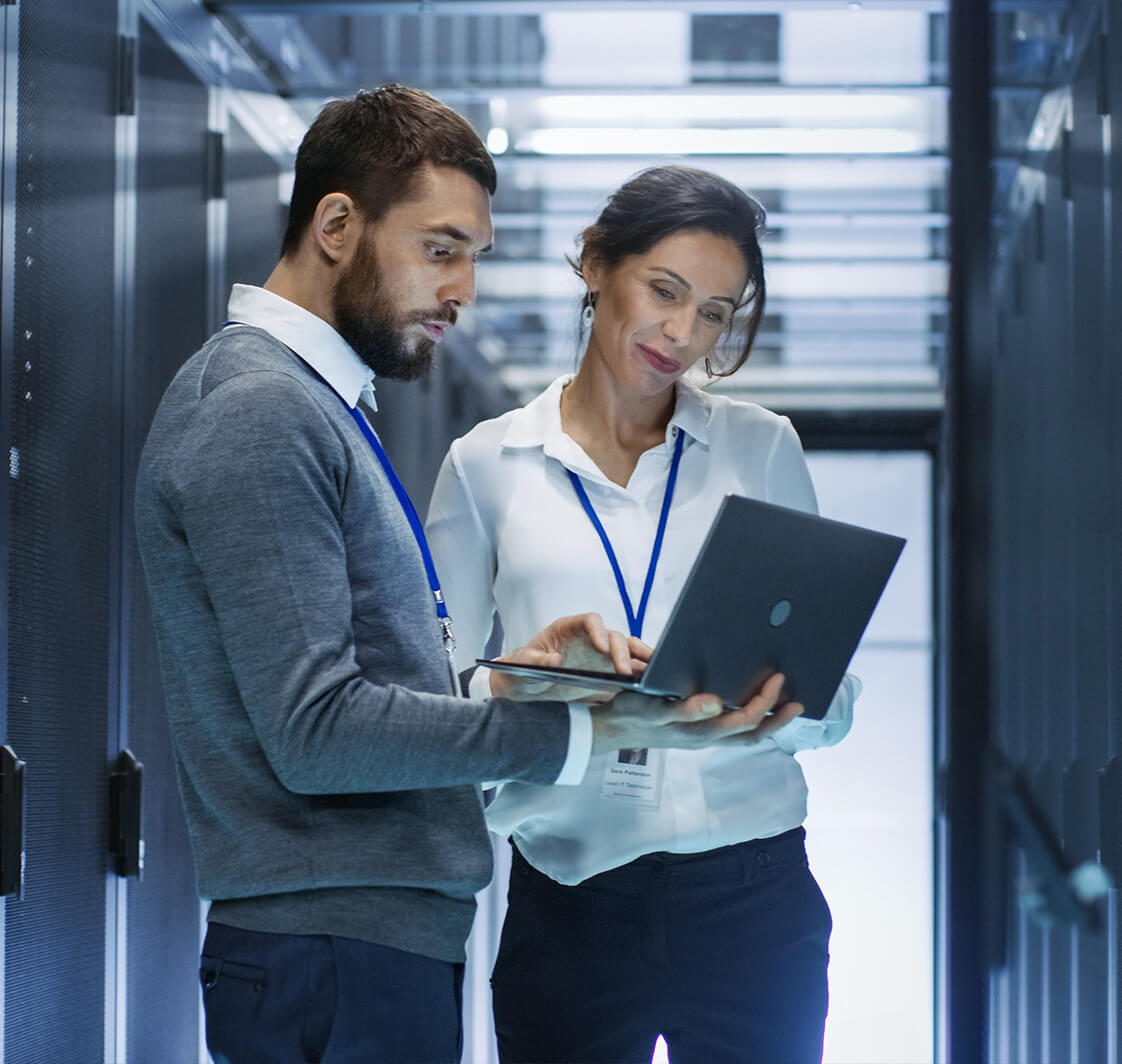 Male IT Specialist Holds Laptop and Discusses Work with Female Server Technician. They're Standing in Data Center, Rack Server Cabinet is Open.