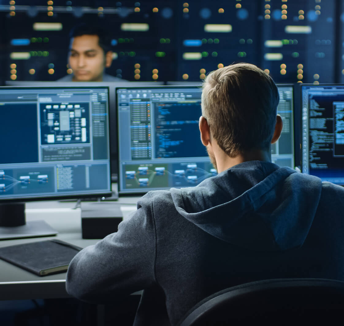 IT Specialist Works on Personal Computer with Screens Showing Software Program with Coding Language Interface. In the Background Technical Room of Data Center with Professional Working.