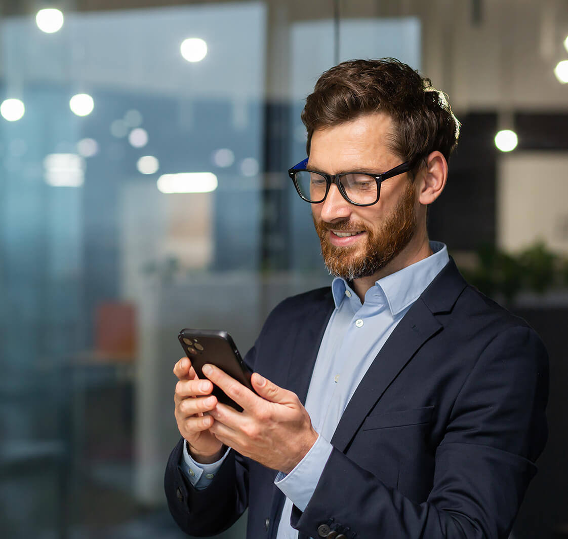 Businessman in business suit uses mobile near window.