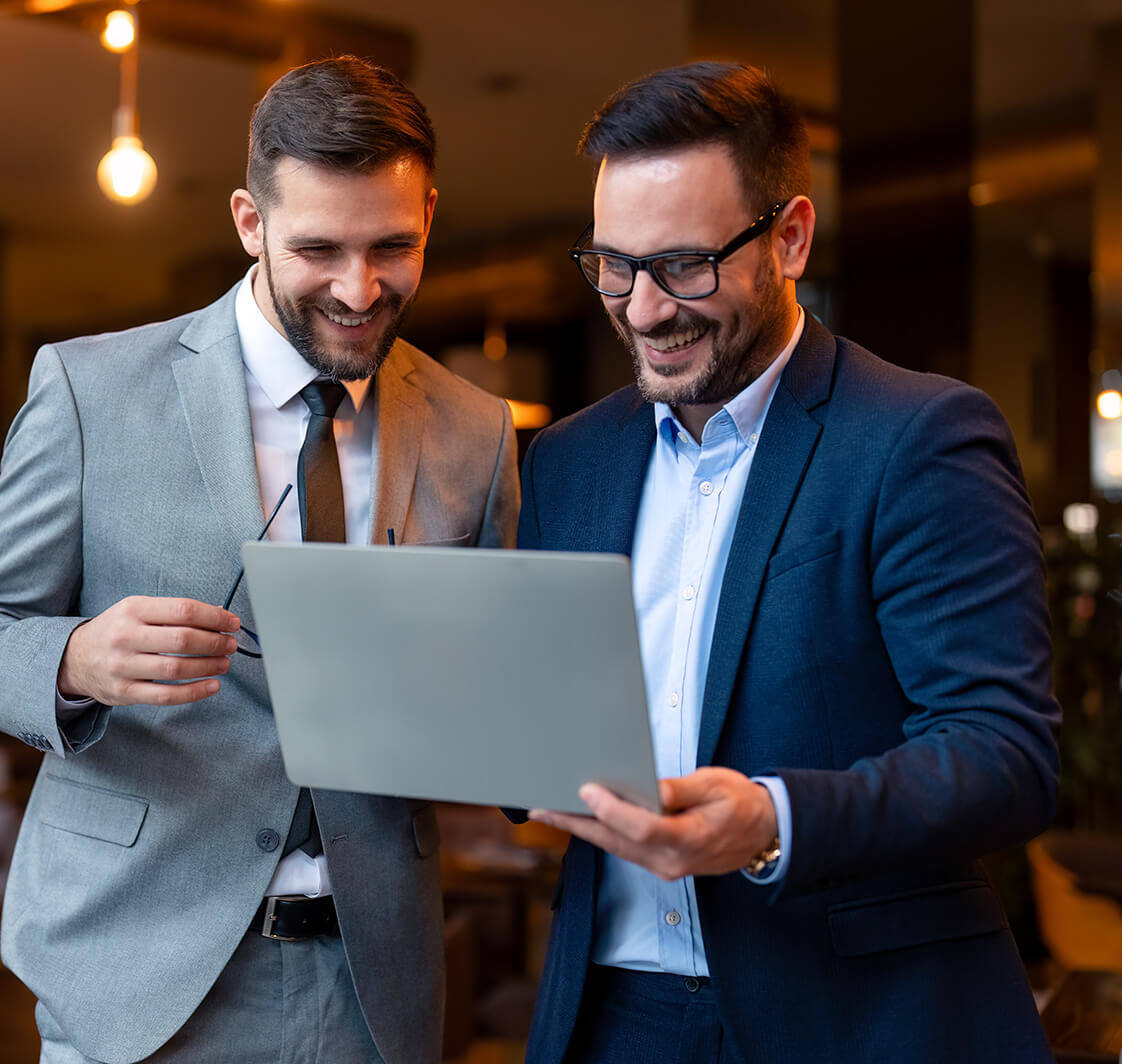 Two satisfied business men looking at a slideshow presentation on a laptop in a co-working space.