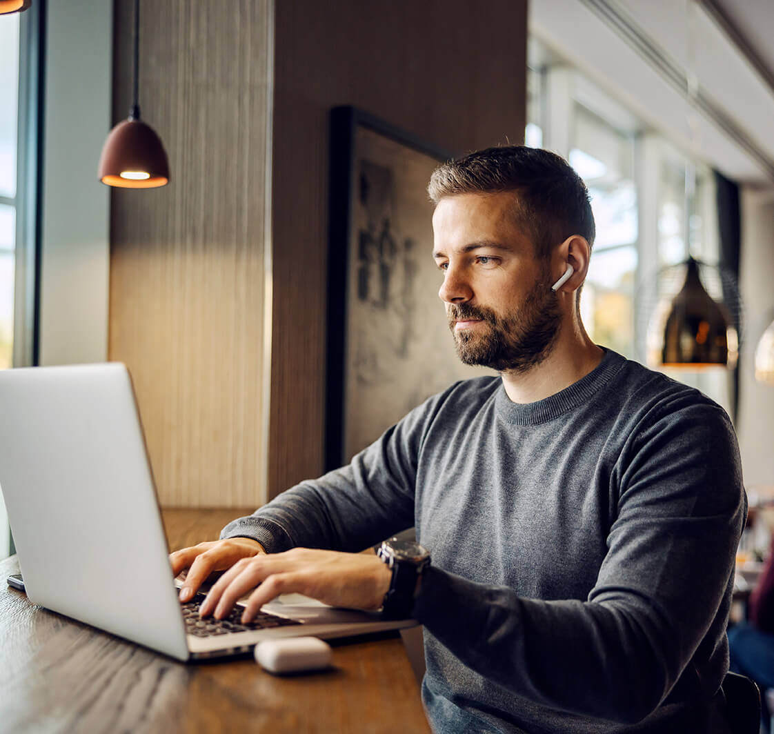 A freelancer is sitting at cafeteria and typing report on a laptop while working remotely.