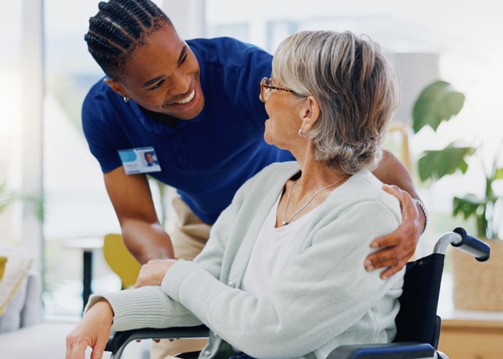 Male community nurse crouched down talking with a female patient in a wheelchair.