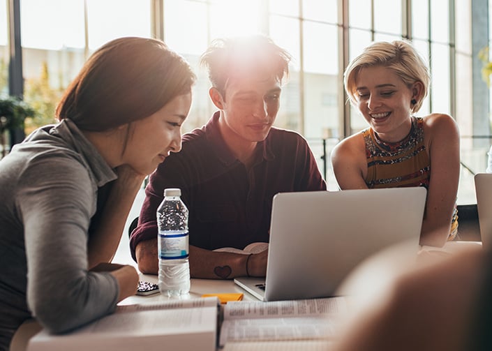 Three education and research institute students sitting at a table with research books and are all looking at a laptop screen.