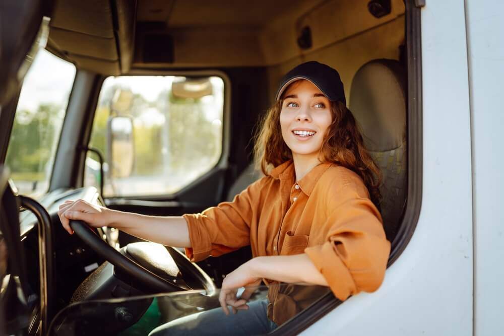 Female lorry driver in the driver's seat, smiling.