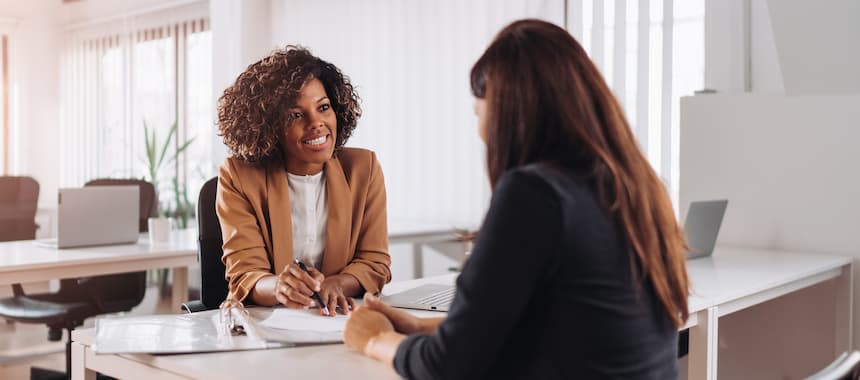 Smiling women sat at a bank desk working together as a partnership on cyber security