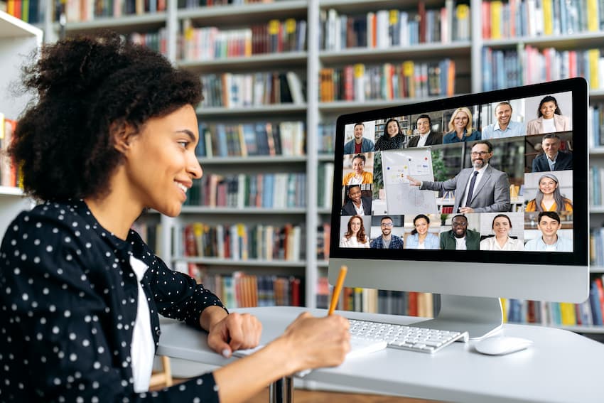 A smiling teacher in the school library, looking at her colleagues and students online in a Teams meeting.