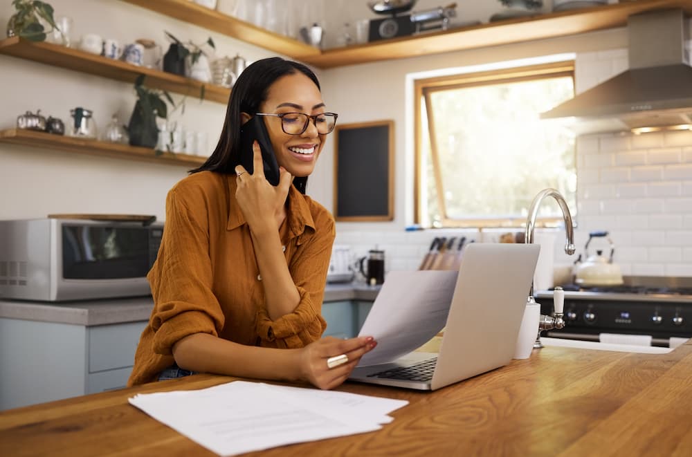 Remote worker smiling while on the phone sat at her kitchen table with her laptop