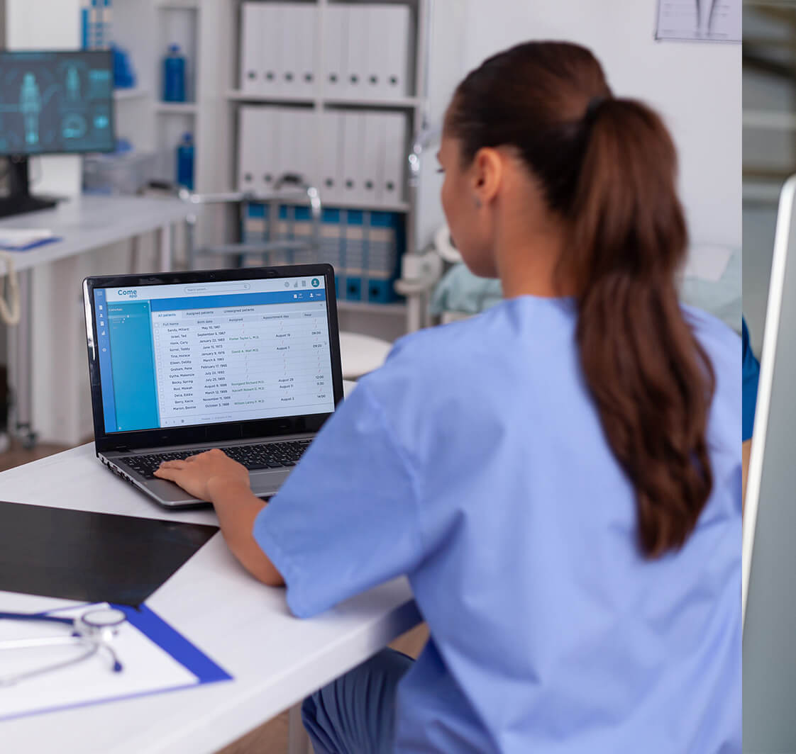 Medical nurse checking patient documentation on laptop in hospital office.