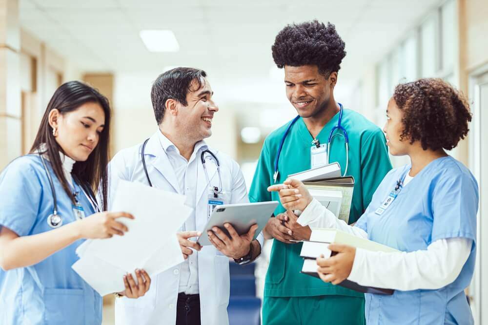 Four student doctors are stood discussing files in a teaching hospital